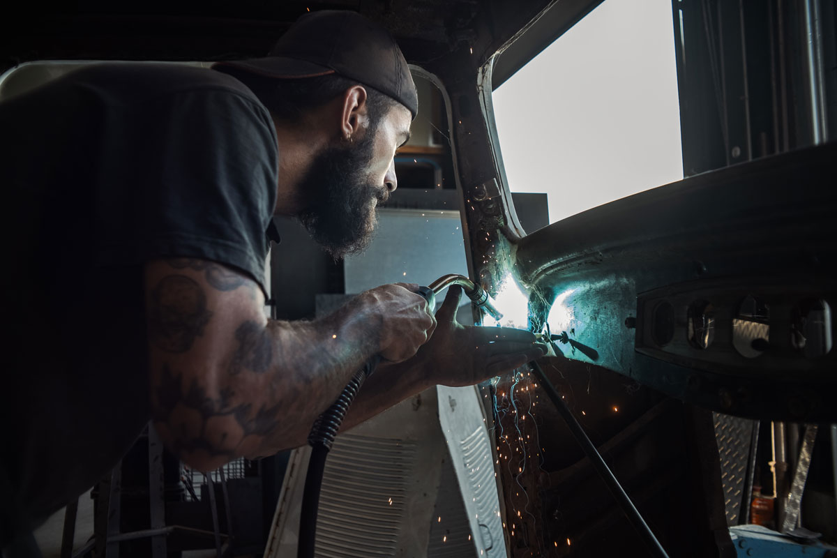 Un technicien soude l'intérieur d'une portière d'une voiture de collection